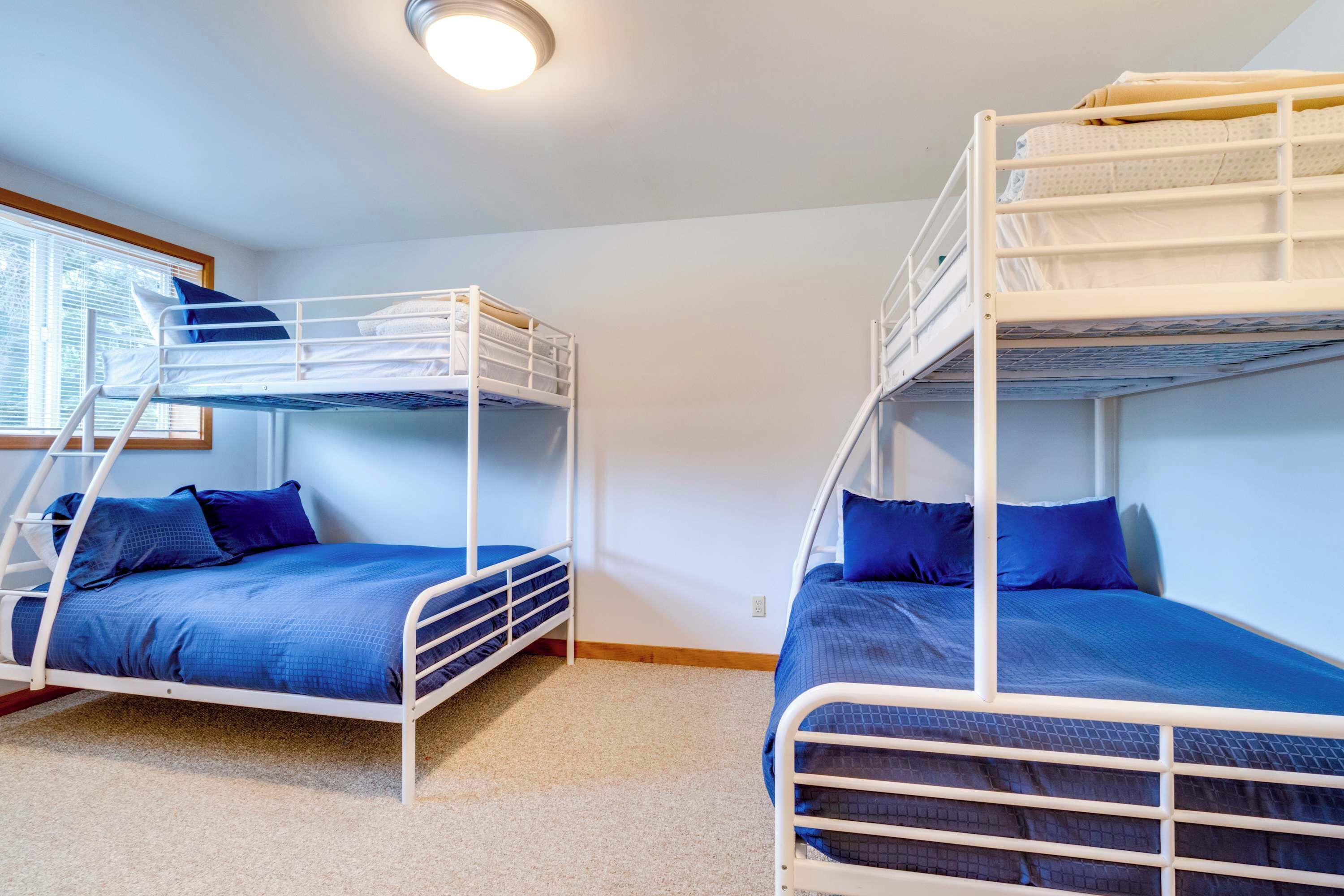 Een kamer met twee stapelbedden, elk met een blauwe matras en kussens, en een raam met zonwering.