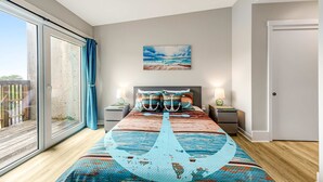 Une chambre à coucher avec un grand lit, deux tables de chevet avec des lampes, un tableau représentant la mer et une porte-fenêtre coulissante donnant sur l’extérieur.