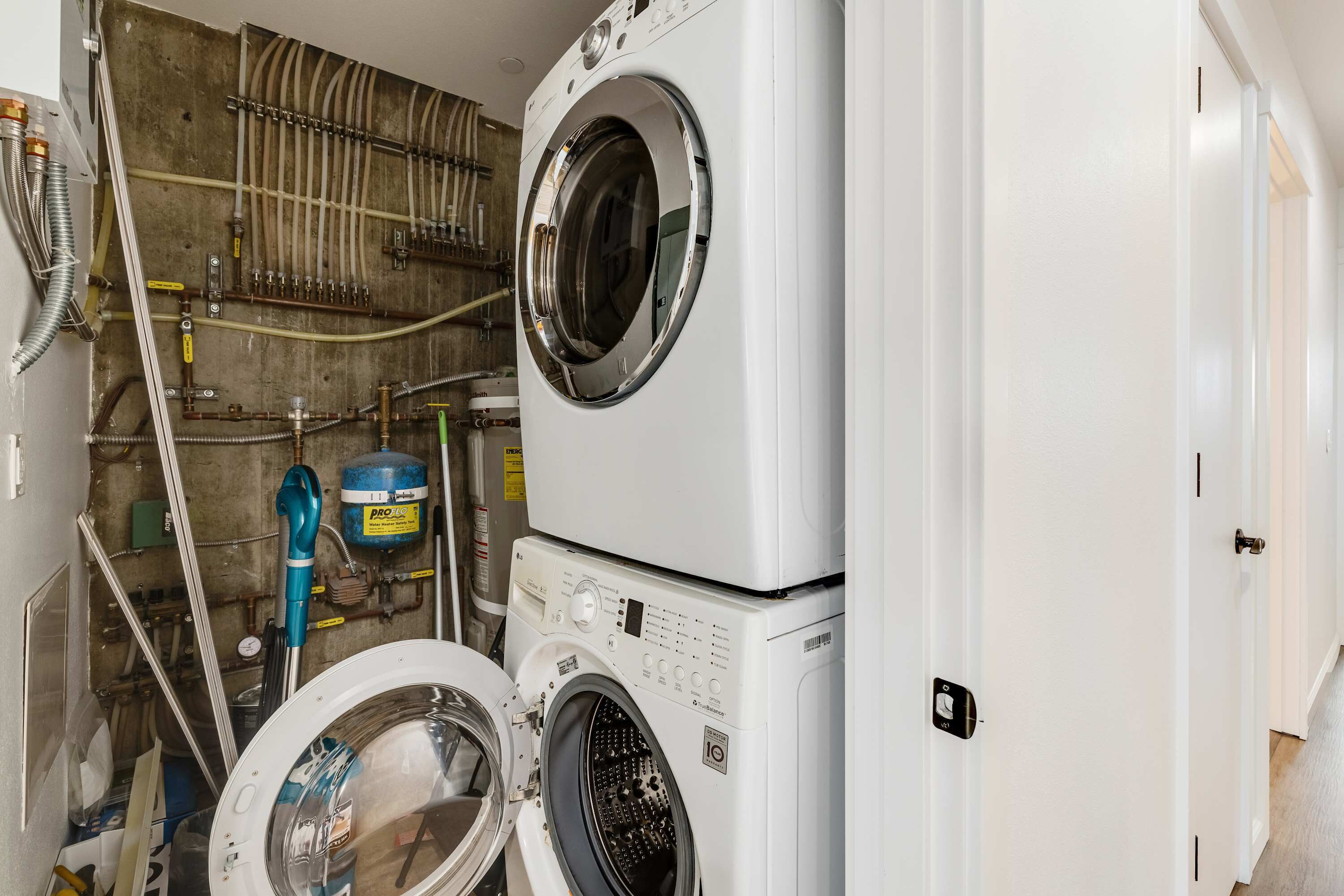 Een wasserette met twee gestapelde wasmachines, een boiler en diverse leidingen en slangen.