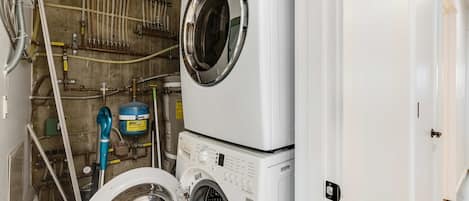 Een wasserette met twee gestapelde wasmachines, een boiler en diverse leidingen en slangen.