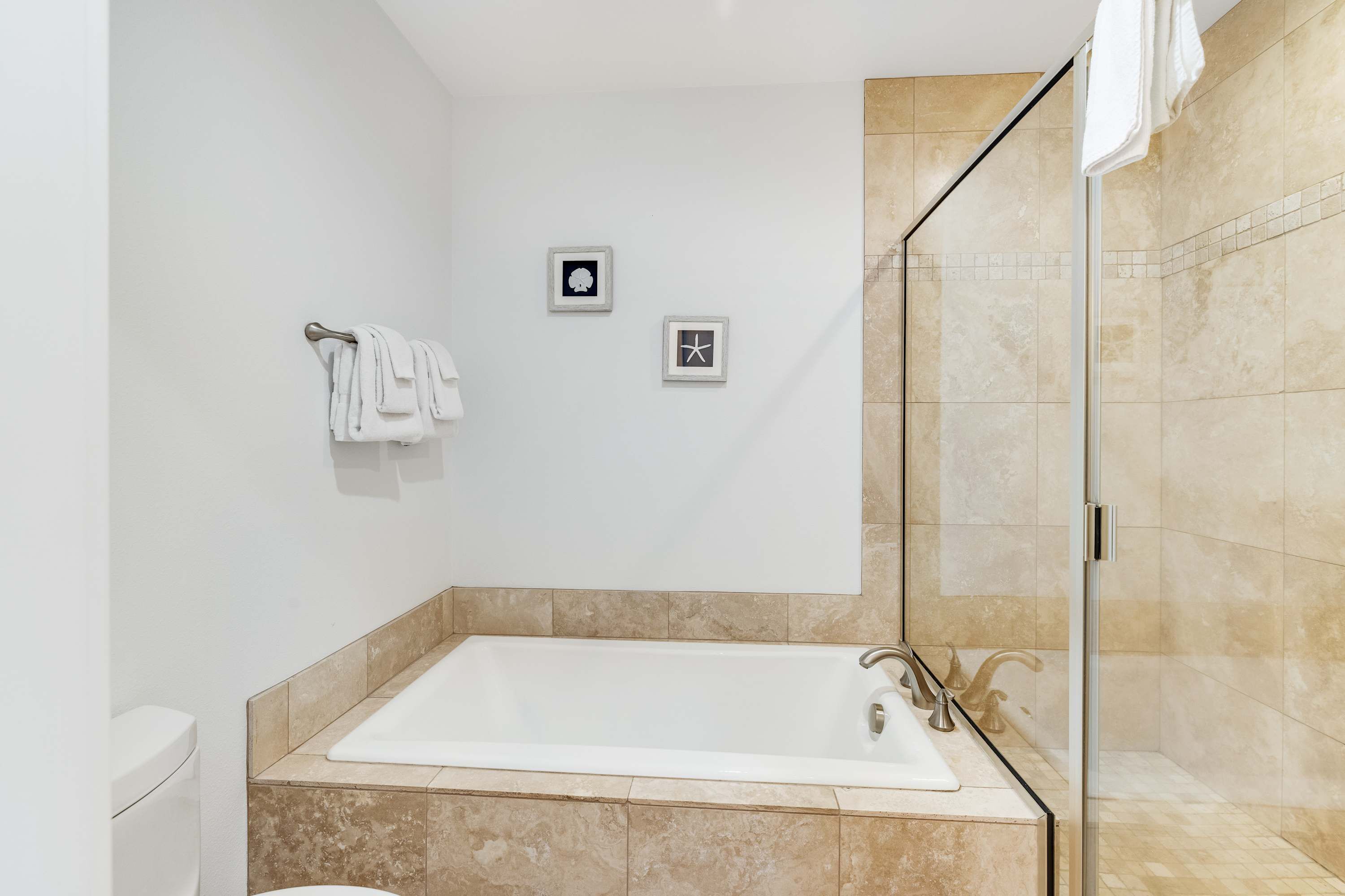 Un baño moderno con una bañera grande, una ducha con mampara de vidrio y dos cuadros en la pared.