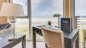 Una stanza con una scrivania, una lampada, una sedia e vista sulla spiaggia.