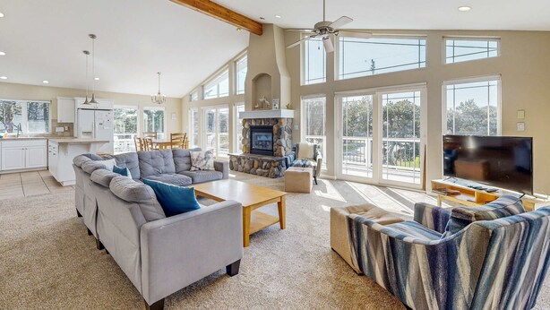 A spacious living room with a fireplace, large windows, and a television. - Ocean side home steps from sand dog friendly (Rockaway Beach)