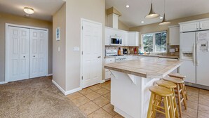 A kitchen with white cabinets, a large island with stools, a microwave, and a refrigerator. - Ocean side home steps from sand dog friendly (Rockaway Beach)