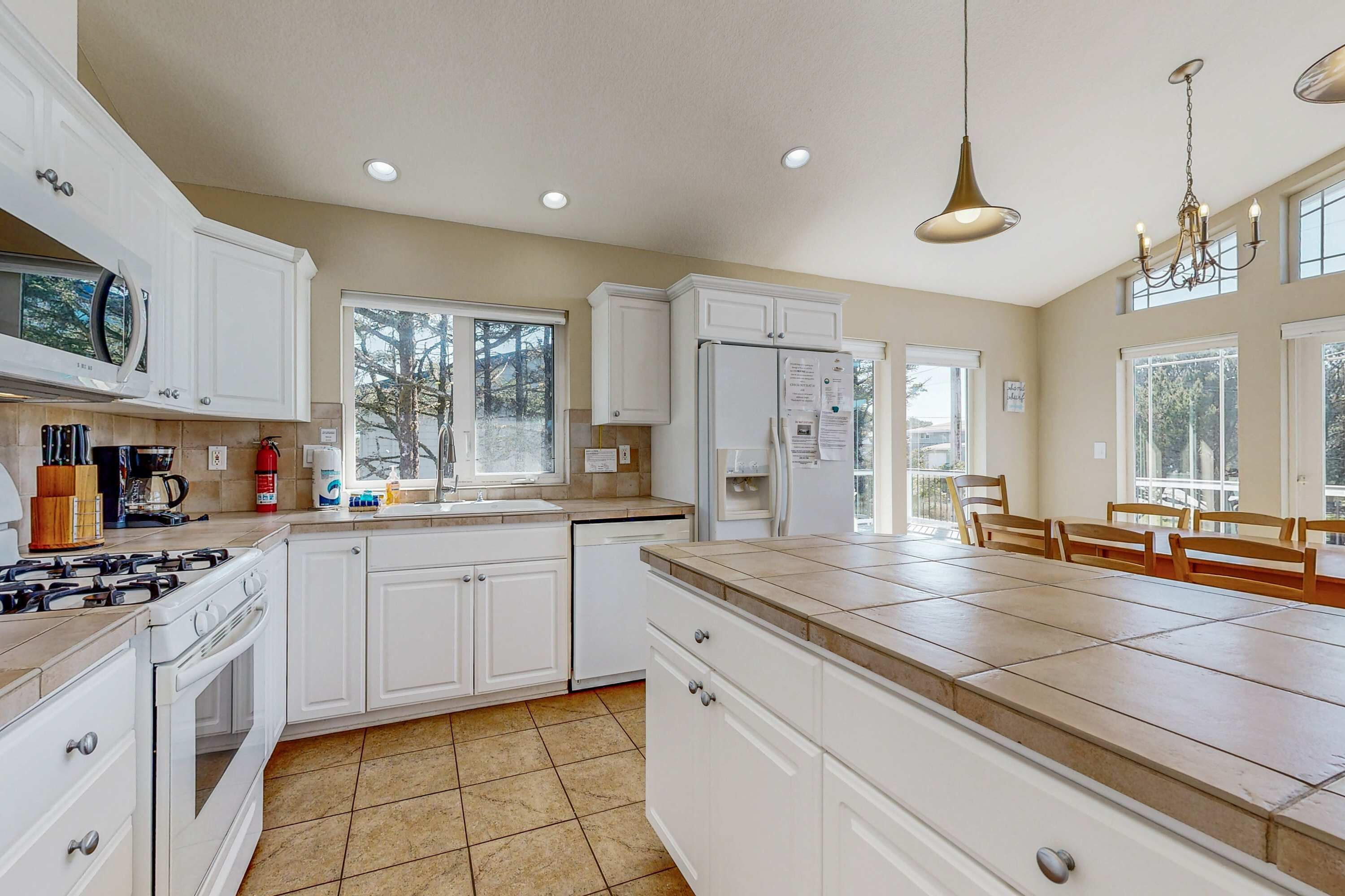 A modern kitchen with white cabinets, a large island, and a dining area with wooden chairs.