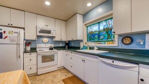 Uma cozinha com armários brancos, micro-ondas, forno, máquina de lavar louça e uma janela com vista para um vitral.
