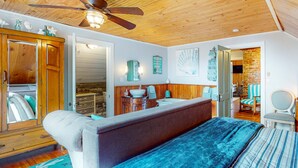 A bedroom with a bed, a wooden ceiling fan, a bathroom with a sink and mirror, and a view of the outside. - Dog Friendly Cottage with Private Hot Tub Close to Beach and Downtown (Rockaway Beach)