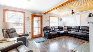 A living room with a leather sectional sofa, a wooden ceiling, and a door with a sign. - Dog Friendly Cottage with Private Hot Tub Close to Beach and Downtown (Rockaway Beach)