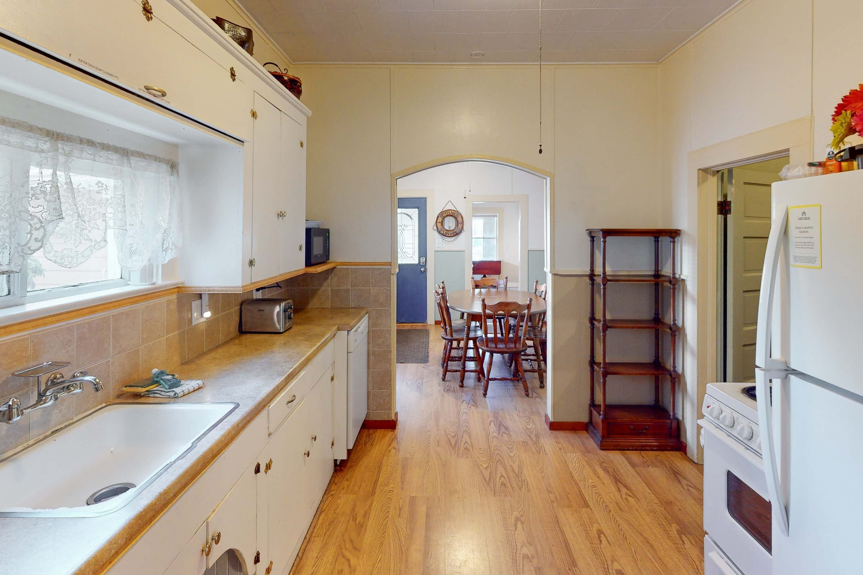A kitchen with wooden flooring, white cabinets, a sink, and a stove.