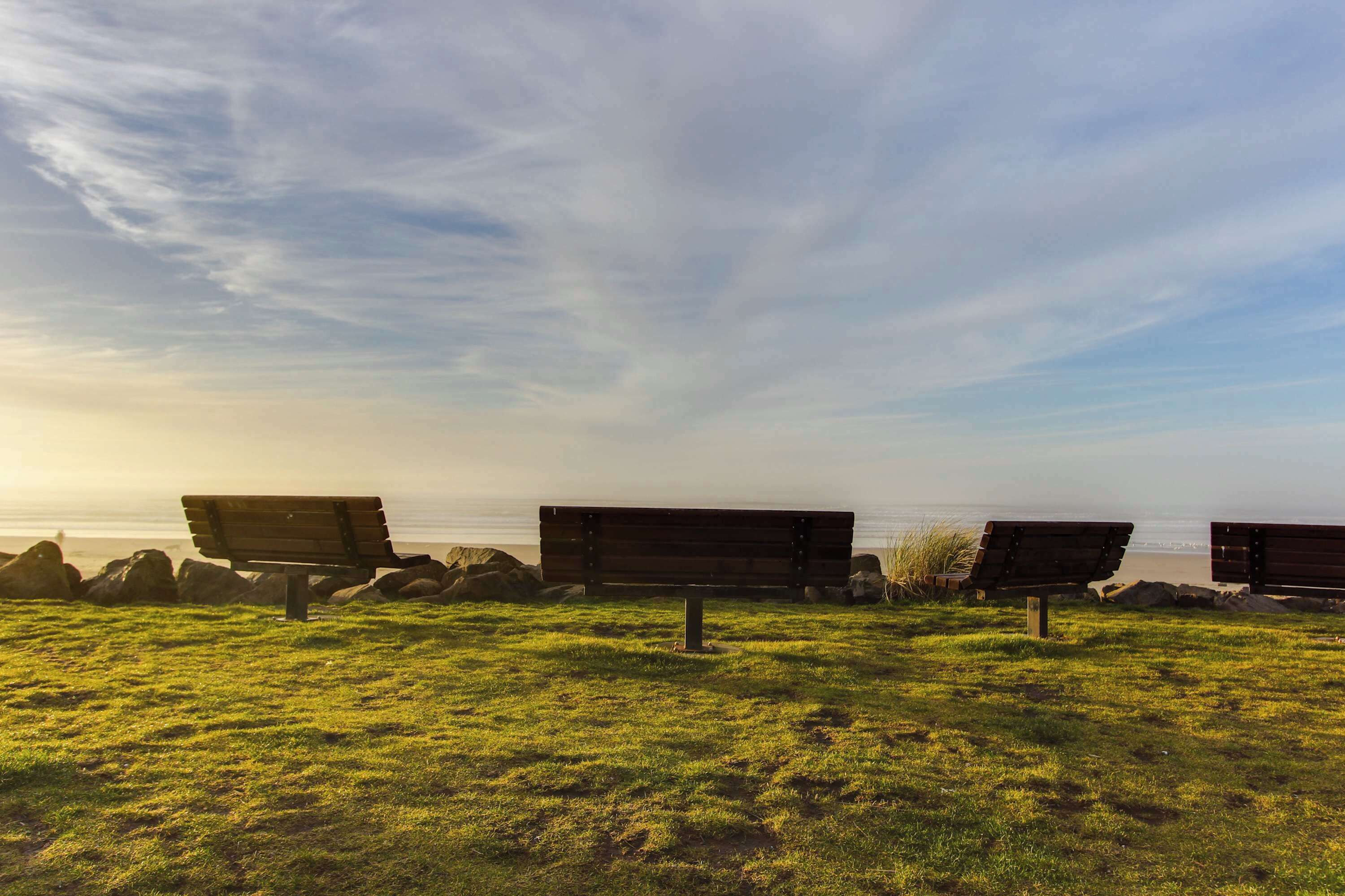 Three wooden benches on a grassy field with a view of the ocean.
