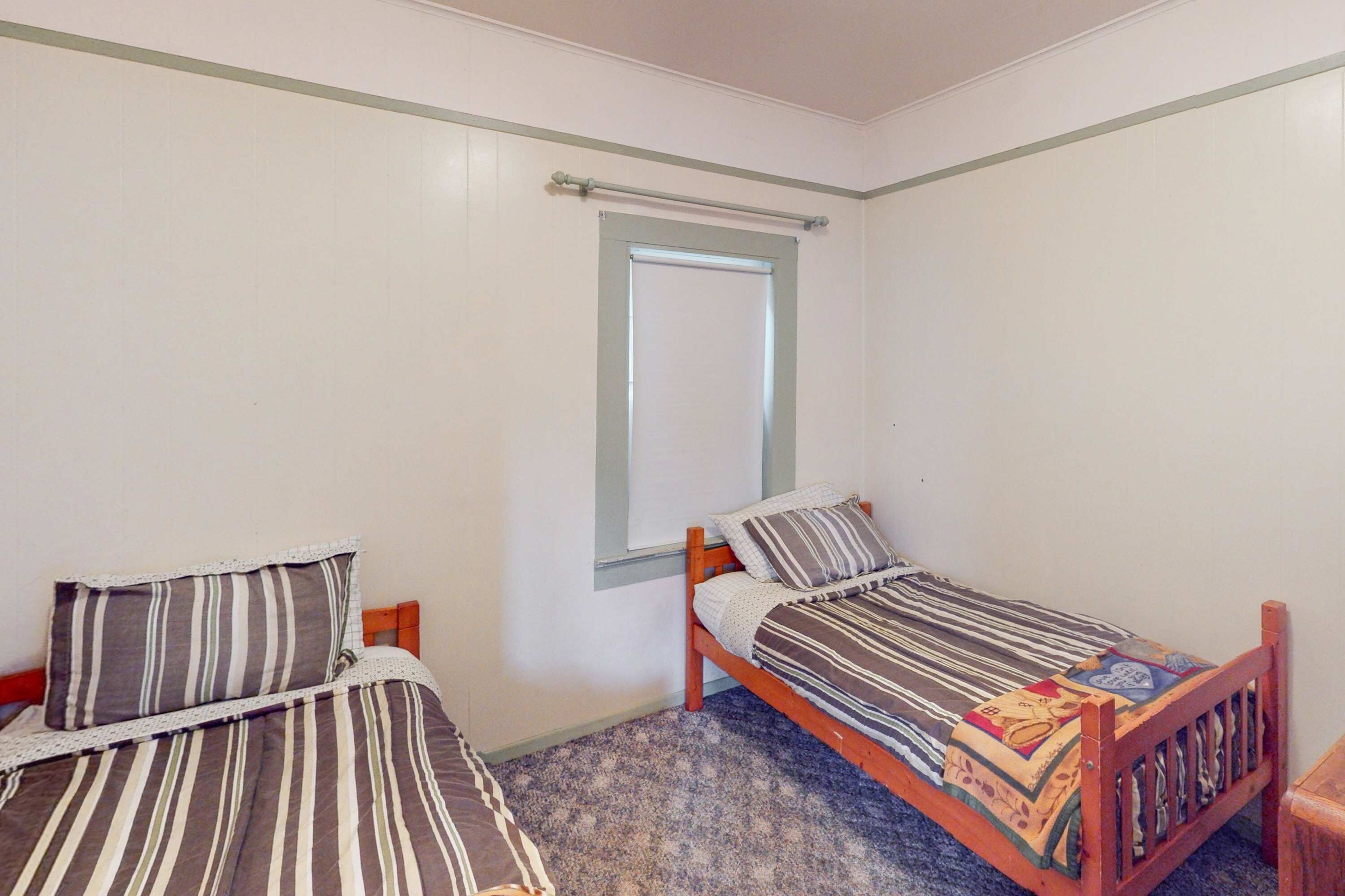 Une chambre avec deux lits simples, une fenêtre et une tête de lit en bois.