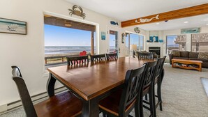 Een ruime woonkamer met een grote houten eettafel, comfortabele zitplaatsen en uitzicht op het strand.