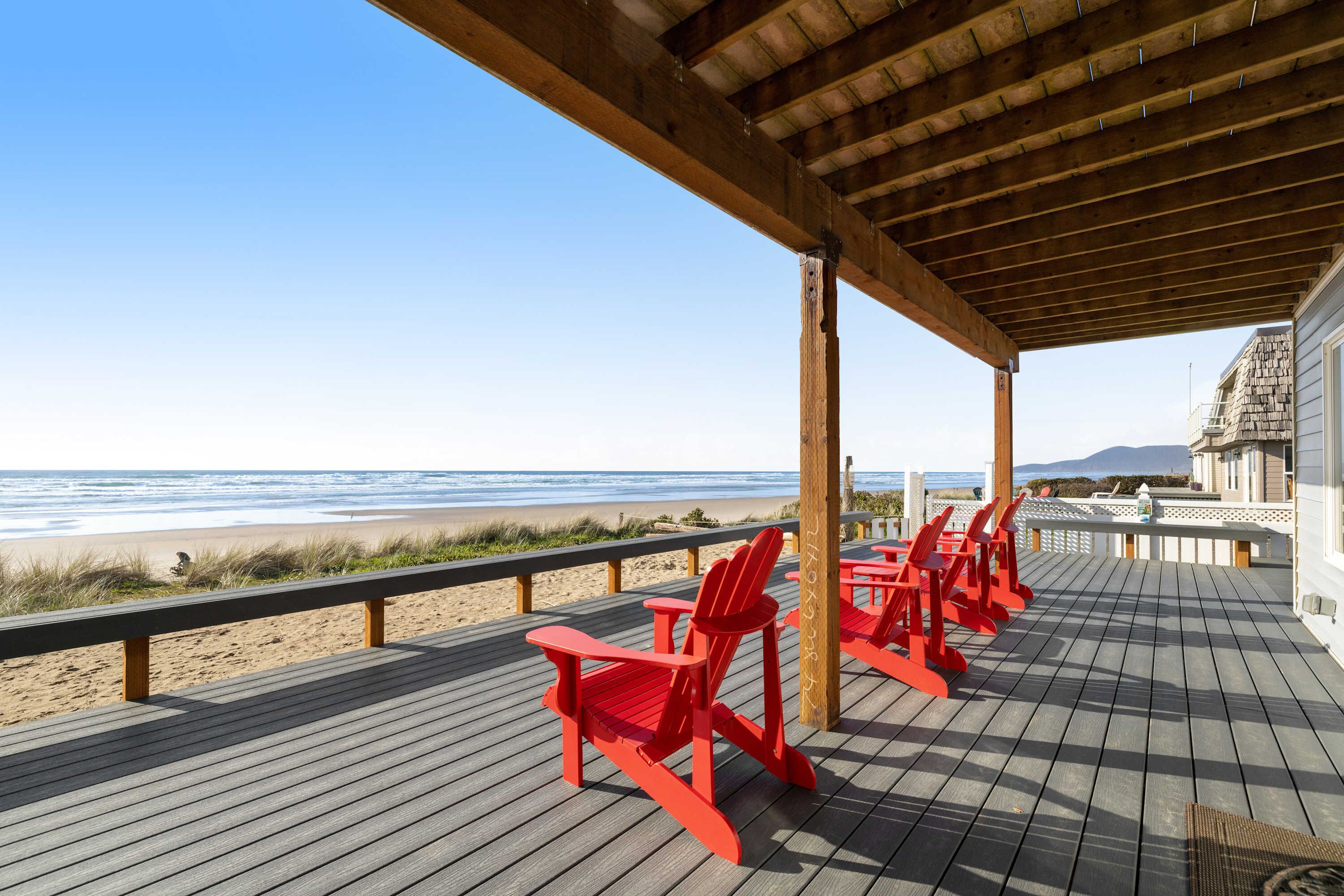 Une terrasse en bois avec des fauteuils Adirondack rouges donnant sur une plage.