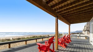 Een houten terras met rode Adirondack-stoelen met uitzicht op een strand.