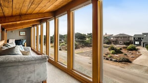 A room with a large window, a gray sofa, and a wooden ceiling. - Dog friendly home across street from beach with rooftop deck and views (Rockaway Beach)