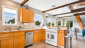 A kitchen with wooden cabinets, a dishwasher, an oven, and a sink. - Dog friendly home across street from beach with rooftop deck and views (Rockaway Beach)