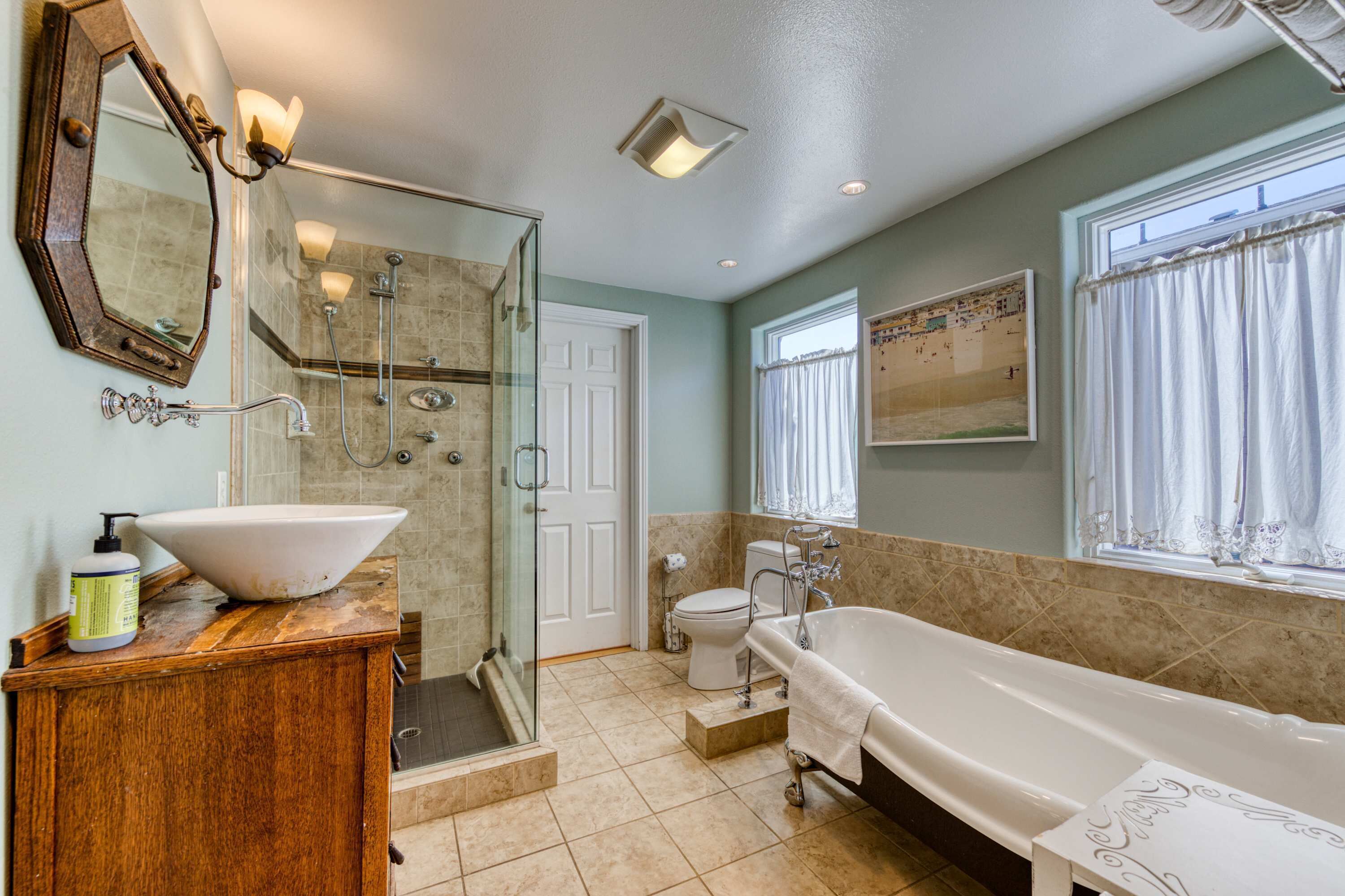 Une salle de bain dotée d’une douche à parois de verre, d’une grande baignoire blanche, d’un meuble-lavabo en bois avec un vasque et d’un grand miroir.