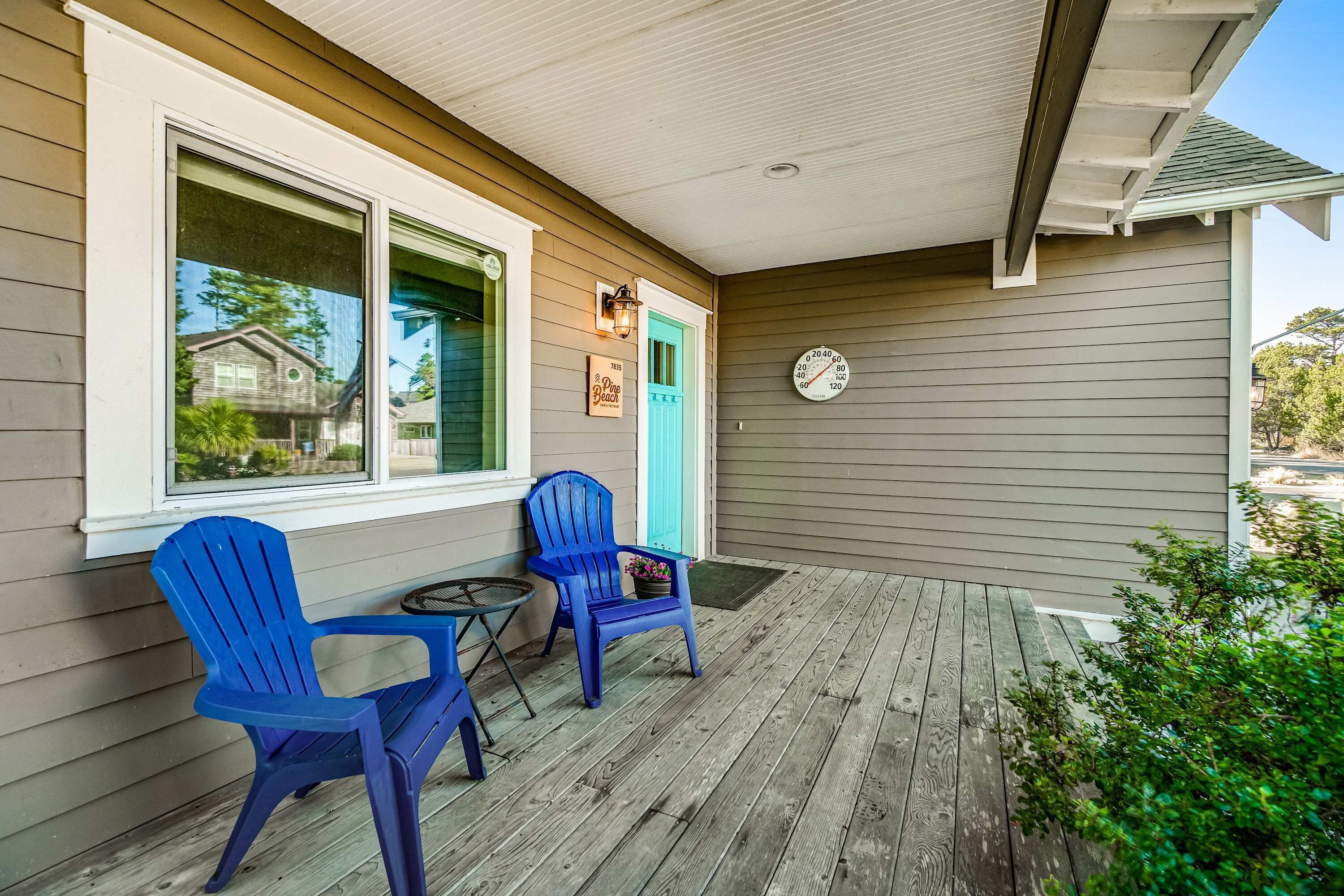 A porch with two blue Adirondack chairs, a small round table, and a clock on the wall.