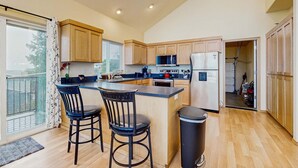 Een moderne keuken met houten kastjes, een centraal eiland met barstoelen, een magnetron, kookplaat en koelkast.