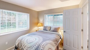 A bedroom with a bed, two windows, a door, and a nightstand with a lamp. - Cozy family home away from home dog friendly with nearby beach access and hot tub (Rockaway Beach)
