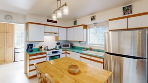 A modern kitchen with white cabinets, a wooden dining table, a stainless steel refrigerator, and a microwave. - Cozy family home away from home dog friendly with nearby beach access and hot tub (Rockaway Beach)