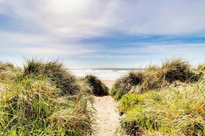 Een zandpad langs duinen begroeid met gras, dat naar de oceaan leidt.