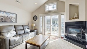 Ein Wohnzimmer mit grauem Ledersofa, einem Holztisch, einem Kamin und einem großen Fenster mit Blick auf die Stadt.