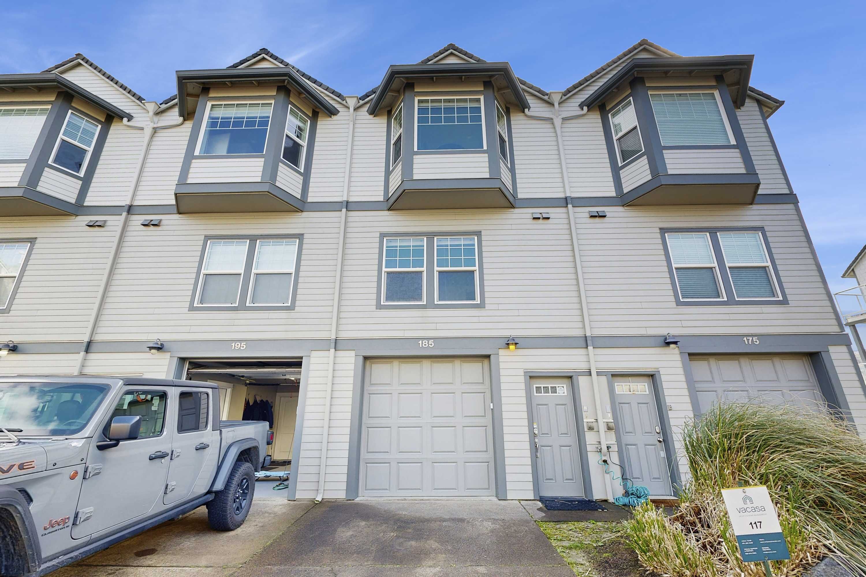 A multi-story residential building with numbered garage doors, a parked Jeep, and a 'Vacasa' sign indicating short-term rental availability.