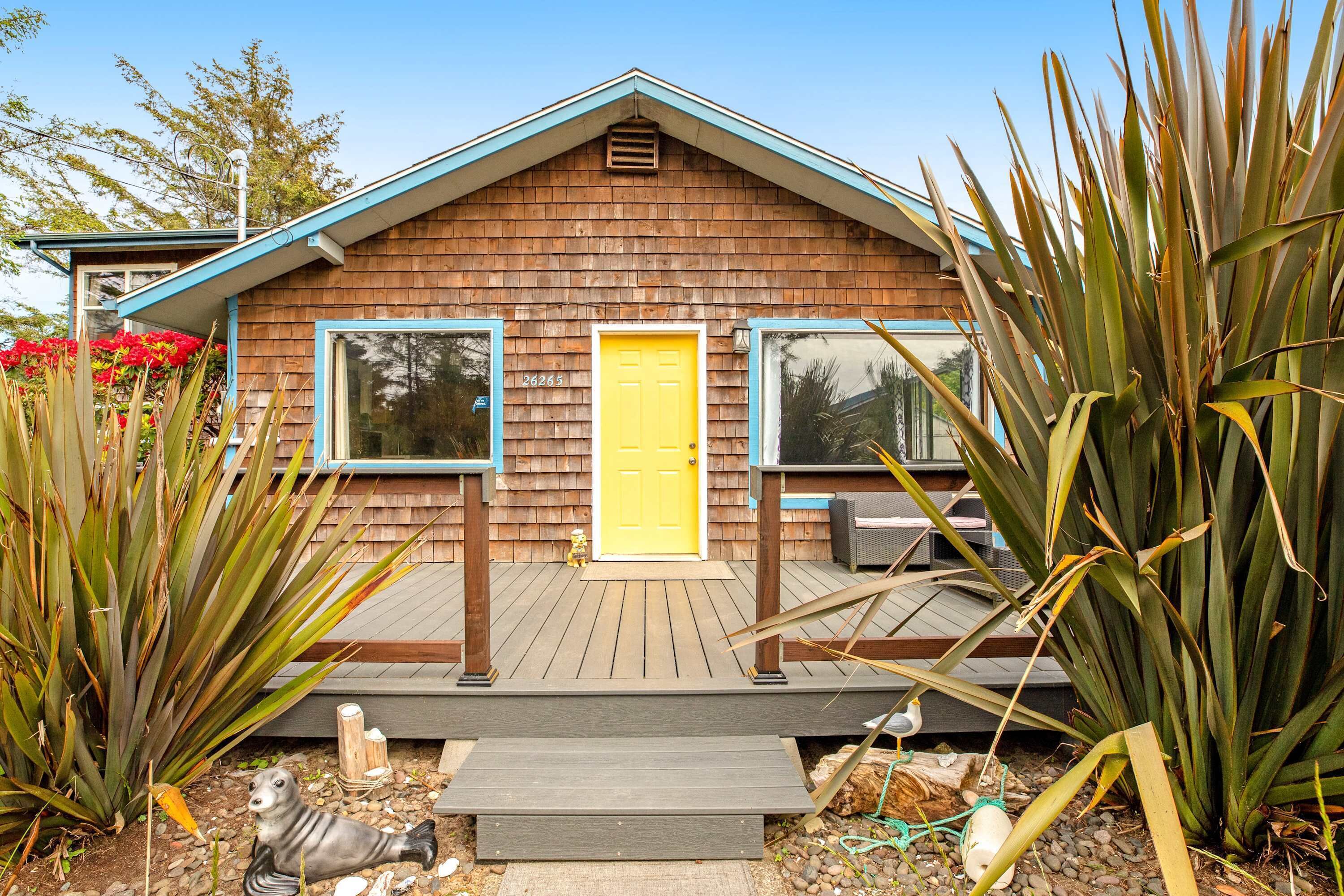 Een houten huis met een gele deur, een veranda en een klein beeldje.