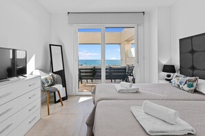 Quarto moderno com uma cama grande, TV, cômoda e varanda com vista para o mar.