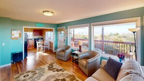 A spacious living room with a large window, a balcony, and a kitchen area. - Family Friendly Oceanfront Condo with Free WiiFi Ocean Views and Easy Beach Access (Rockaway Beach)