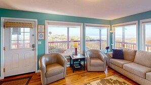 A living room with a beige sofa, two armchairs, a wooden coffee table, and a rug. There are large windows with a view of the beach and a balcony with a railing. - Family Friendly Oceanfront Condo with Free WiiFi Ocean Views and Easy Beach Access (Rockaway Beach)
