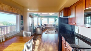 A modern kitchen with wooden cabinets, a black refrigerator, and a dining area with a wooden table and white chairs. - Family Friendly Oceanfront Condo with Free WiiFi Ocean Views and Easy Beach Access (Rockaway Beach)