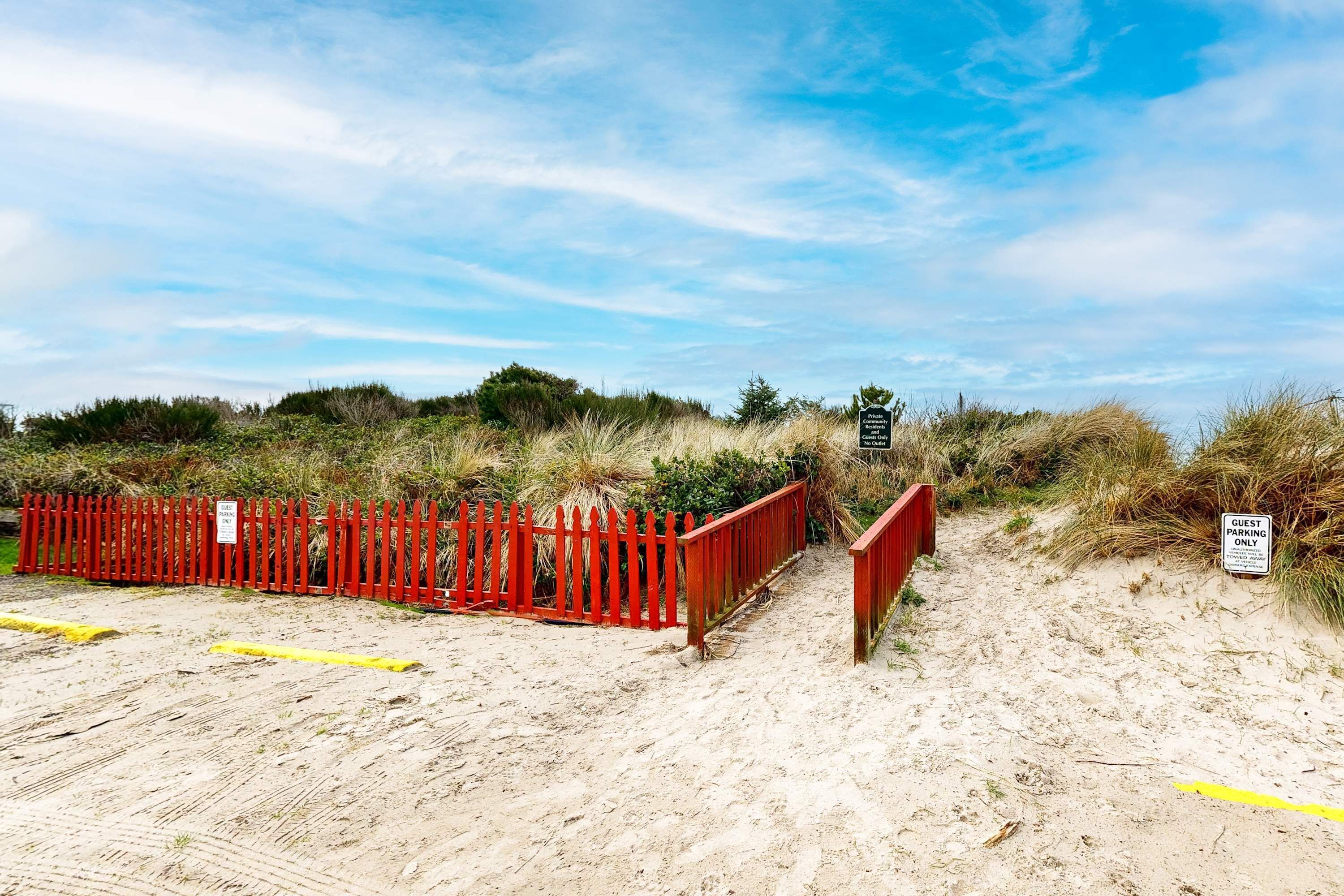 A sandy beach area with a red fence and a sign indicating guest parking.