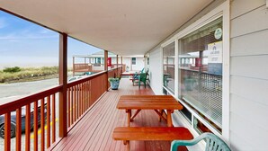 Eine überdachte Terrasse im Freien mit Holztischen und -stühlen, einem Geländer und Blick auf den Strand.