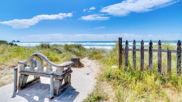Un banc et une clôture en bois, le tout situé près d’une plage, sous un ciel dégagé.