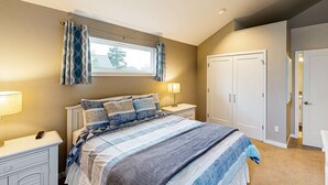 A bedroom with a bed, nightstands, a window with curtains, a wardrobe, and a door. - New House in Quiet Location with Modern Amenities near Beach Lake and Town (Rockaway Beach)