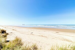 A beach with sand and grass in the foreground, a clear sky, and a calm sea. - New House in Quiet Location with Modern Amenities near Beach Lake and Town (Rockaway Beach)