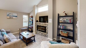 A living room with a fireplace, a bookshelf, and a television. - New House in Quiet Location with Modern Amenities near Beach Lake and Town (Rockaway Beach)