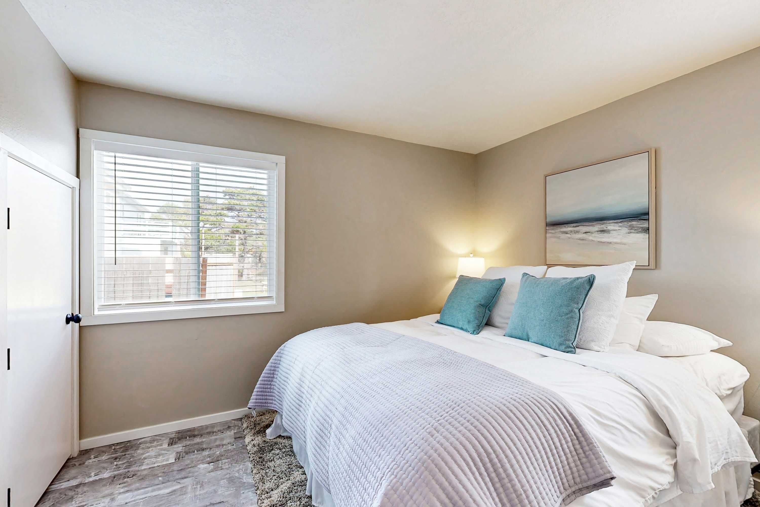 A bedroom with a bed, a window, and a painting on the wall.