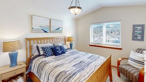 Una camera da letto con un letto, comodini, una sedia, una finestra e opere d'arte alle pareti.