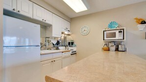 A modern kitchen with white cabinets, a granite countertop, a microwave, a toaster, and a clock on the wall. - Oceanfront condo with a full kitchen balcony and sweeping sea views (Rockaway Beach)