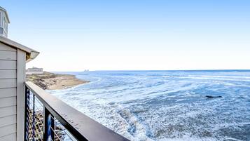 A coastal view from a balcony with a railing, overlooking a beach and ocean.