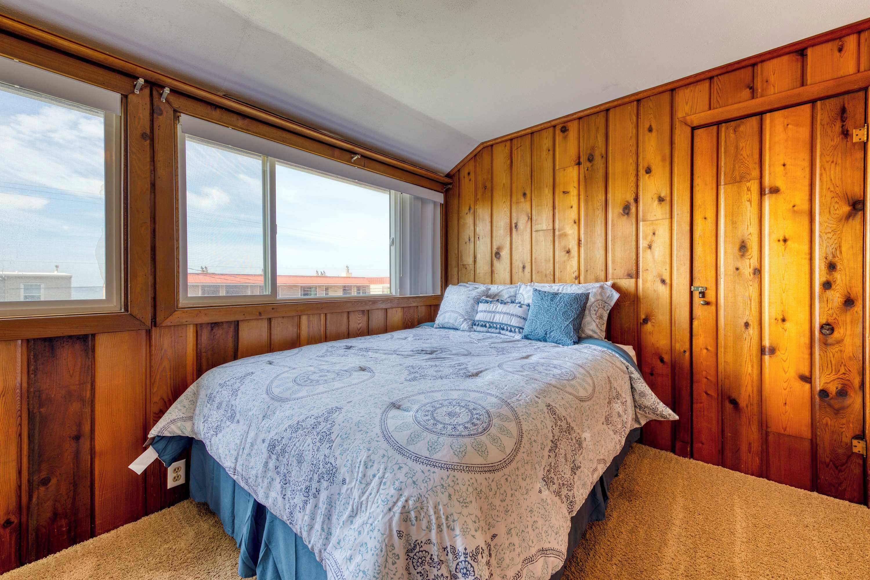 Quarto com uma cama grande, paredes de madeira e uma janela com vista para edifícios.