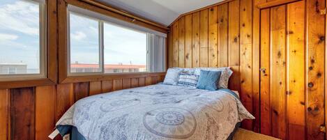Quarto com uma cama grande, paredes de madeira e uma janela com vista para edifícios.