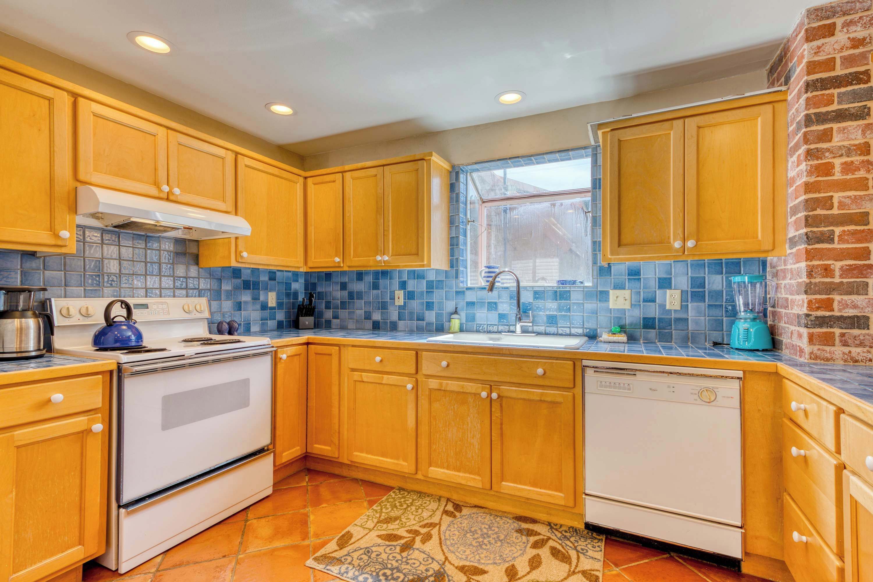 A kitchen with wooden cabinets, a white stove, a dishwasher, and a blue tiled backsplash.