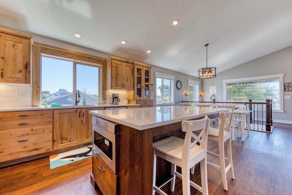 A modern kitchen with wooden cabinets, a large island, and bar stools. - Newly built home with lake view and game room steps to downtown walk to beach (Rockaway Beach)