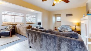 A living room with a sofa, armchairs, a television, and a ceiling fan. - Ocean view home with prime walkable location near beach and town 2 dogs OK (Rockaway Beach)