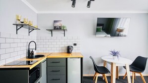 Une cuisine compacte équipée d’un évier, d’une cuisinière et d’un réfrigérateur, un petit coin repas avec une table et des chaises, et un téléviseur fixé au mur.