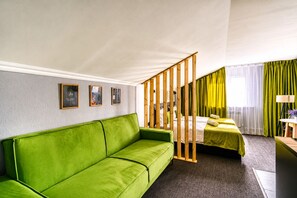 A hotel room with a green sofa, two beds, a wooden partition, and a window with green curtains. - Rise Tokio Hotel  (Almaty)